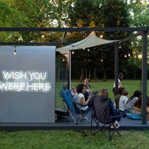 starting a glamping business in the UK with Garden Pods | Image: Side view of grey garden Pod with neon sign reading Wish You Were Here, family enjoying the outdoors