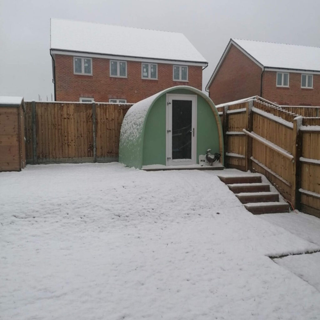 Cosy, small garden Pod in green during winter, covered in snow 