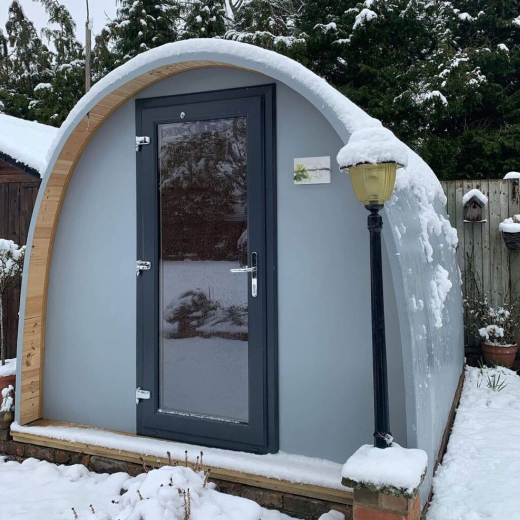 A cosy winter garden room in silver grey, covered in snow | Hully Pods 