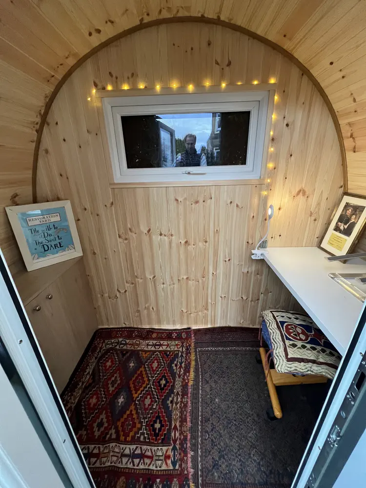 Pine interior of Alexander's Dory Office Pod with a desk, rug and fairy lights