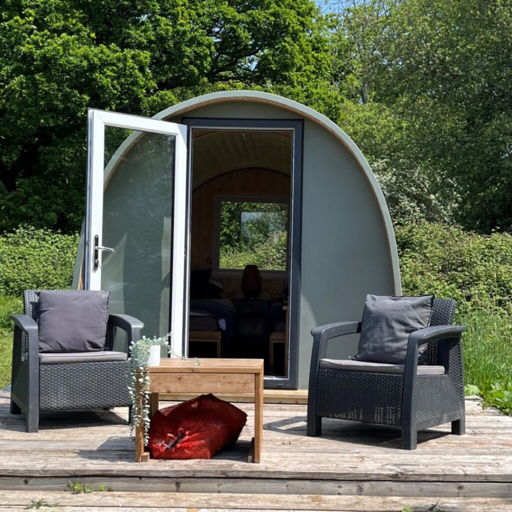 Starting a Glamping Business: Standard Campsite Size | Image Description: Gray Glamping Pod with glass door opening onto deck with two wicker chairs and a table